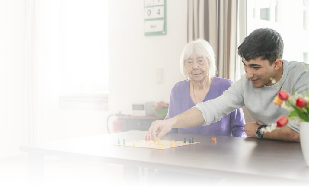 Seniorin und junger Mann spielen gemeinsam ein Brettspiel im Pflegezentrum Lichtenberg.
